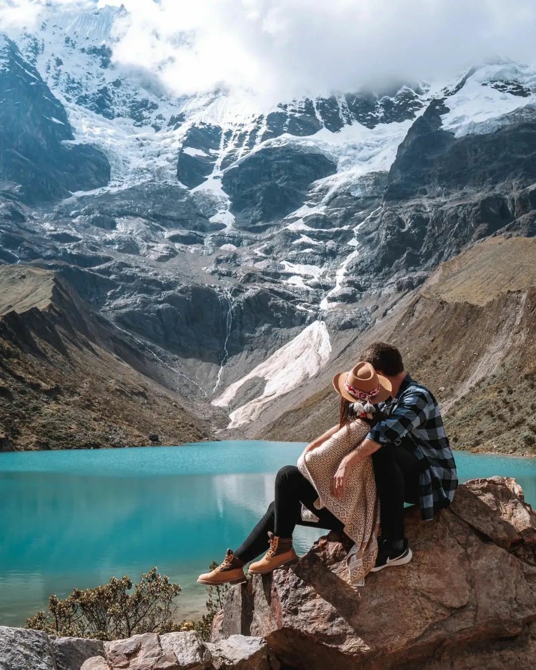 Reflejo azul-turquesa de la Laguna Humantay bajo el cielo andino, rodeada de picos nevados y terreno rocoso.